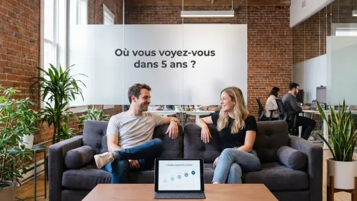Entretien dans un open-space de startup : échange détendu sur un canapé autour d’une feuille de route de carrière à 5 ans, la question affichée sur une cloison vitrée.
